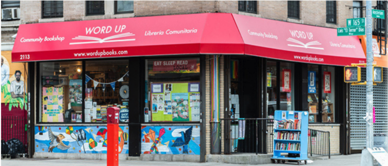 Image of the front of Wordup Community Bookshop, shown from a corner view with red awnings