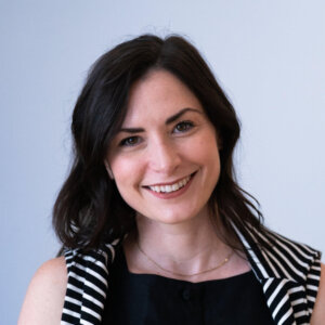 white woman with dark hair wearing a black shirt with black and white stripes ontop.